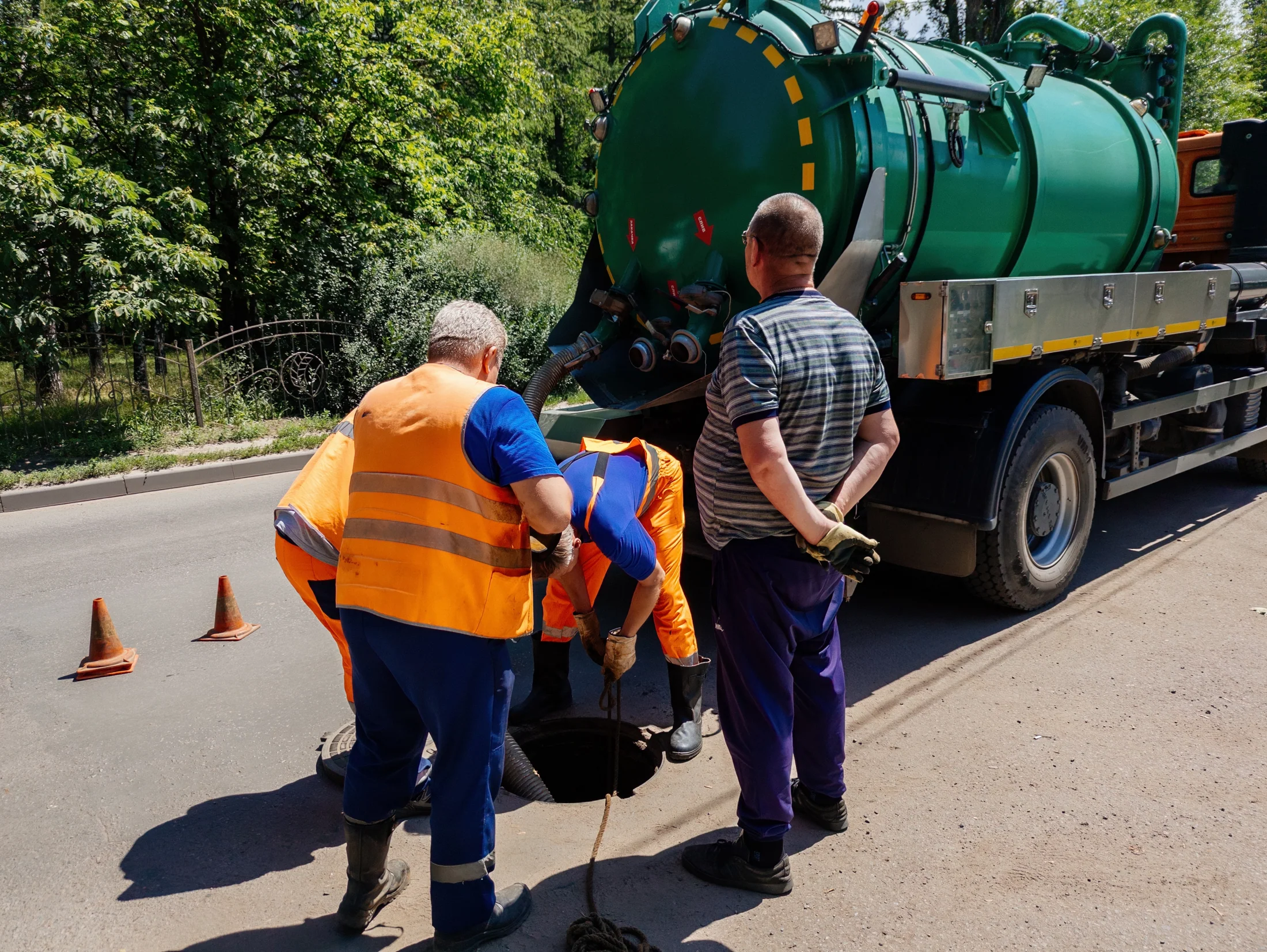 Workers beside a vacuum tanker at a sewer cleaning worksite.