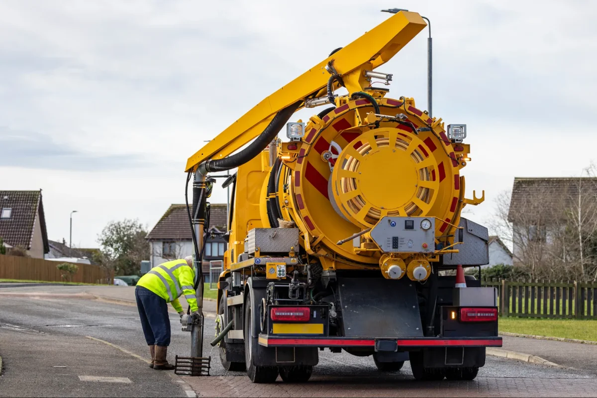 Rear view of a yellow gully-suction tanker and operative at a roadside drain
