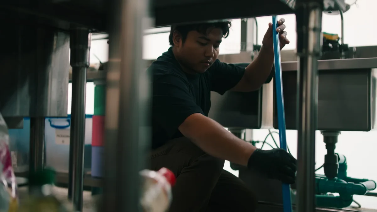 Contractor checking drainage beneath a stainless-steel commercial kitchen sink